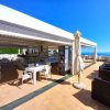 Un bar all'aperto con tavoli bianchi e ombrelloni chiusi su una terrazza soleggiata.