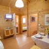 Cucina in legno chiaro con tavolo apparecchiato, porta aperta sul bagno, TV sullo scaffale.
