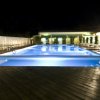 Una piscina illuminata di notte con lettini su una terrazza in legno.