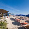 Spiaggia con sdraio e ombrelloni blu e bianchi su sabbia chiara.