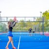 Una donna gioca a padel su un campo blu, circondata da palline, con una rete al centro.