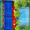 Vista dall'alto di campi sportivi colorati: calcio, paddle e basket, circondati da alberi.