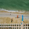 Veduta aerea di una spiaggia con ombrelloni allineati e mare calmo.