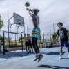 Ragazzi giocano a basket all'aperto, uno in salto tenta un tiro sotto il canestro.