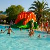 Una piscina all'aperto con uno scivolo gonfiabile arancione e verde, circondata da palme.