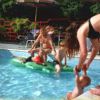 Piscina con adulti e bambini che giocano con un materassino gonfiabile.