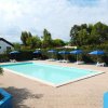 Una piscina rettangolare con sdraio e ombrelloni blu in un'area pavimentata circondata da alberi.