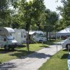 Area campeggio con camper parcheggiati su prato, alberi e un sentiero al centro.