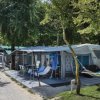 Camper con veranda attrezzata e amaca tra gli alberi lungo un sentiero.