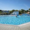 Piscina all'aperto con persone che nuotano. Sullo sfondo, un piccolo scivolo e alberi.