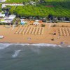 Spiaggia con ombrelloni ordinati, mare in primo piano e area verde sullo sfondo.