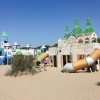Parco giochi sulla sabbia con strutture a tema castello e scivoli colorati sotto un cielo azzurro.